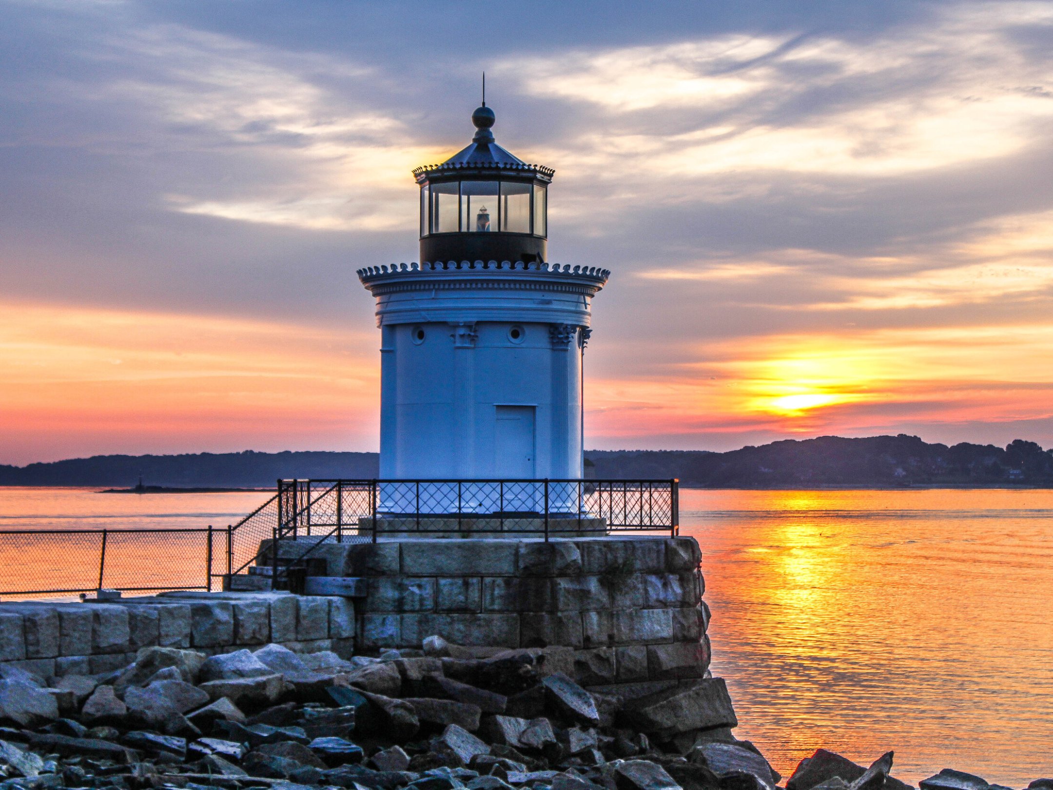 a large clock tower next to a body of water with Portland Breakwater Light in the background