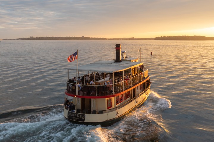 Small ferry with passengers on a river at sunset, American flag waving.