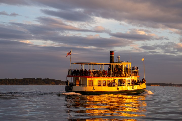 Paddle steamer on a lake at sunset with people on board.