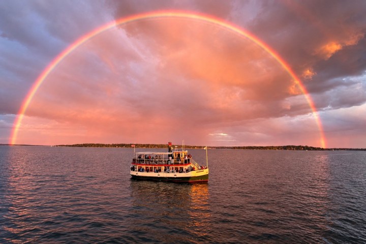 Boat on water under colorful sunset sky with a full rainbow arch.