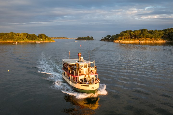 Boat sailing on a calm river surrounded by green islands under a cloudy sky.