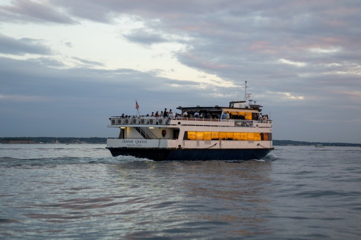Ferry boat on calm water during sunset with cloudy sky.
