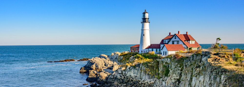 Lighthouse on a rocky cliff by the sea with a clear blue sky.