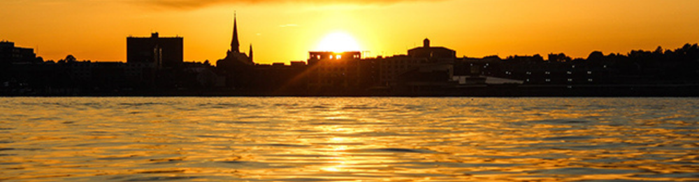 Silhouette of a city skyline at sunset over calm water.