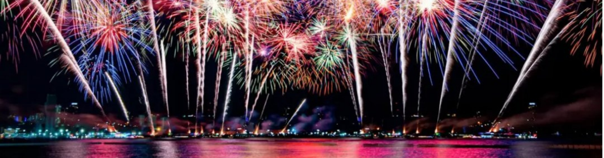 Colorful fireworks exploding over a city skyline and reflecting on water.