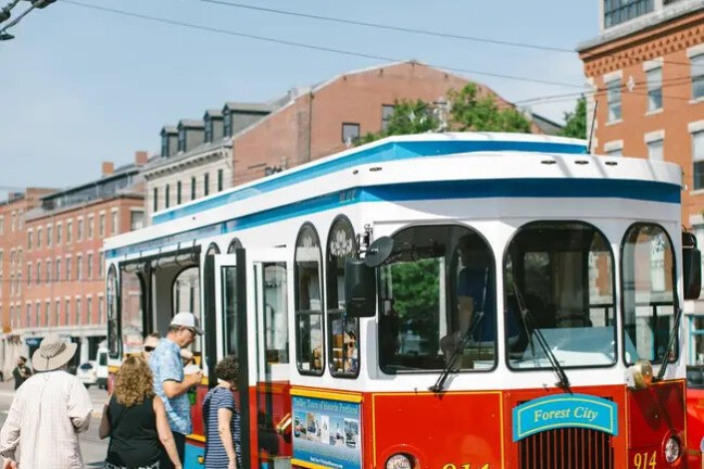 People boarding a colorful trolley on a city street with brick buildings.