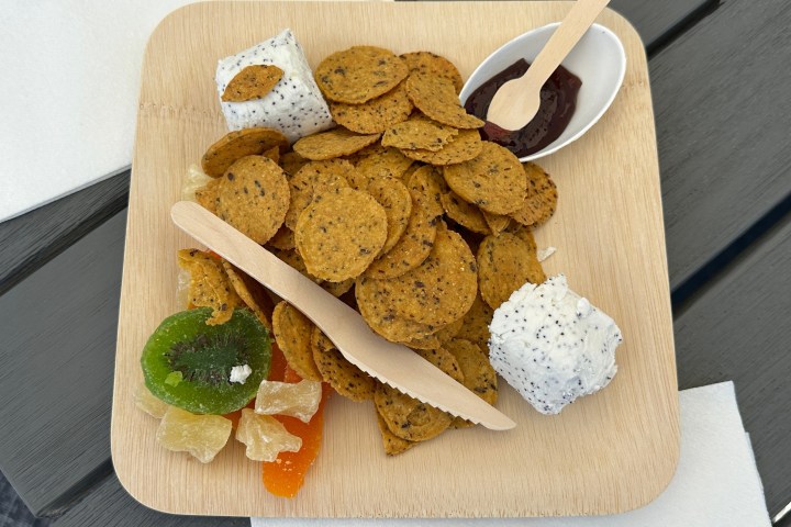 Wooden plate with crackers, cheese balls, dried fruits, and a small sauce dish.