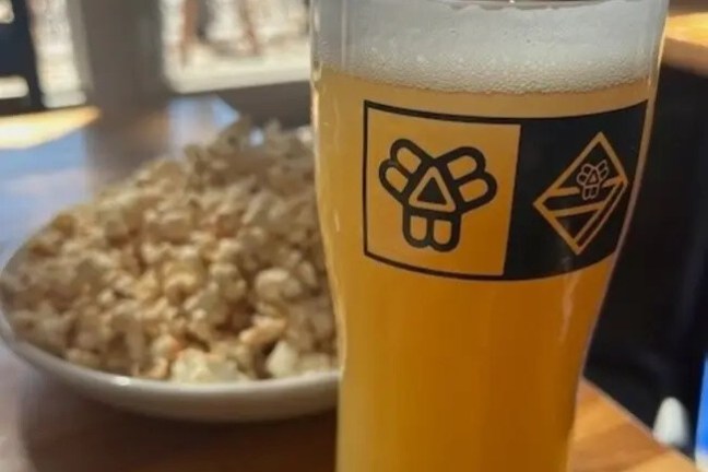 Glass of beer and bowl of popcorn on a wooden table.