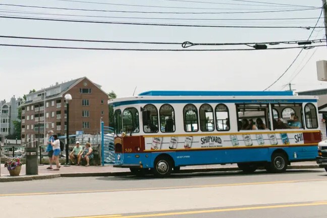 Blue and white trolley labeled 'Shipyard' on a street near brick buildings.