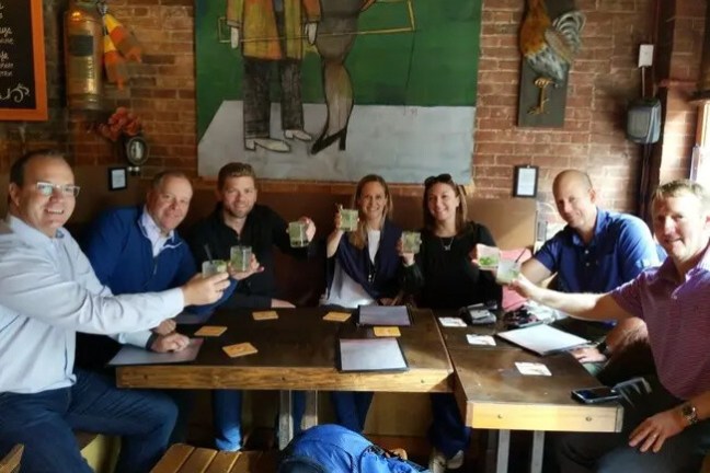 Group of people sitting at a table in a cafe, holding drinks and smiling.