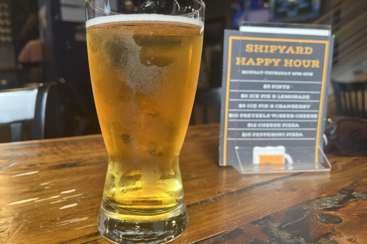 Glass of beer on wooden table near happy hour sign.