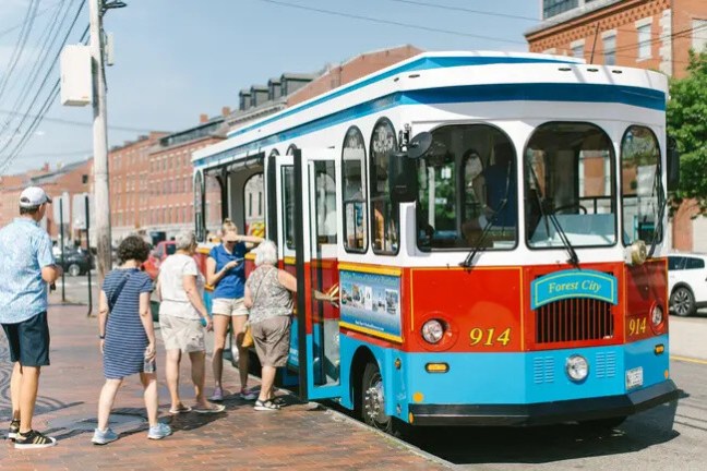 People boarding a colorful trolley on a sunny street.