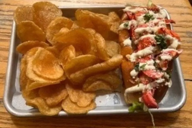 Lobster roll with sauce and herbs, served with chips on a tray.