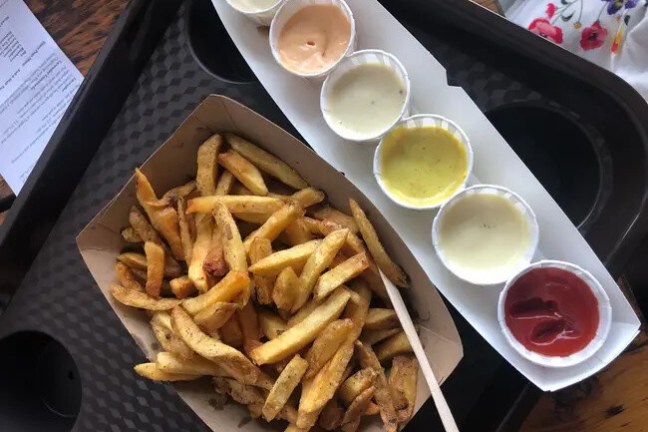 Tray of fries with five dipping sauces in small cups.