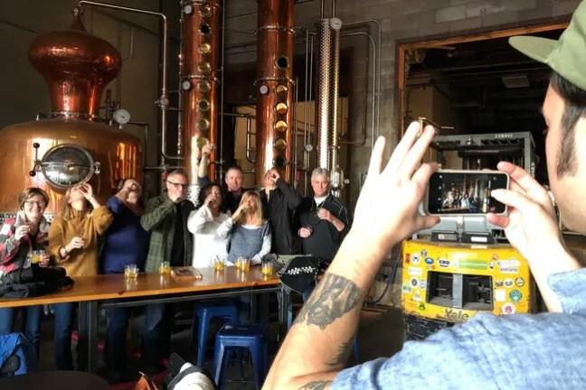 Group of people posing for a photo in a distillery with copper equipment.