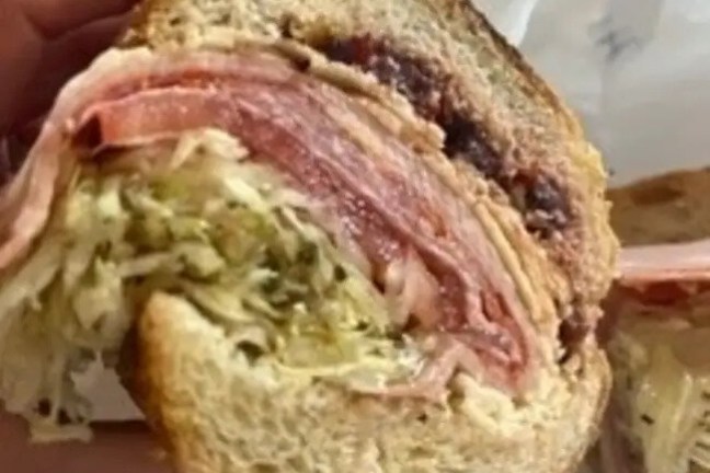 Close-up of a sandwich with layers of meat, cabbage, and dark spread.