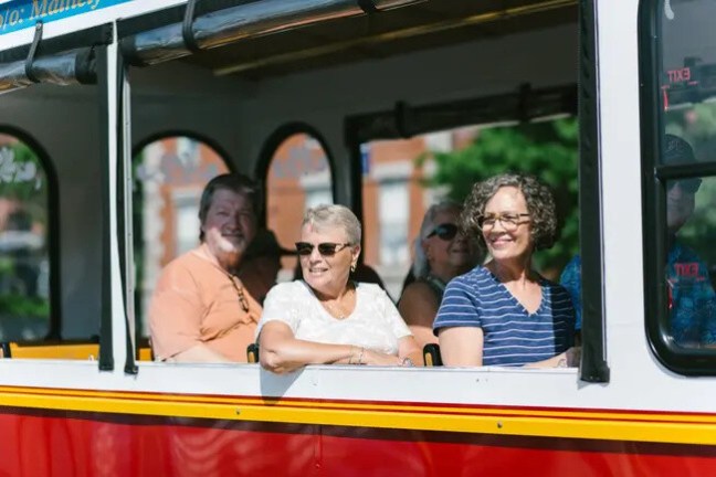 Group of people smiling while sitting inside a red and yellow trolley bus.